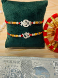 Set of 2 silver-finish metal charm rakhis featuring Om and Ganesh motifs with festive threads – by Wrap Shap.