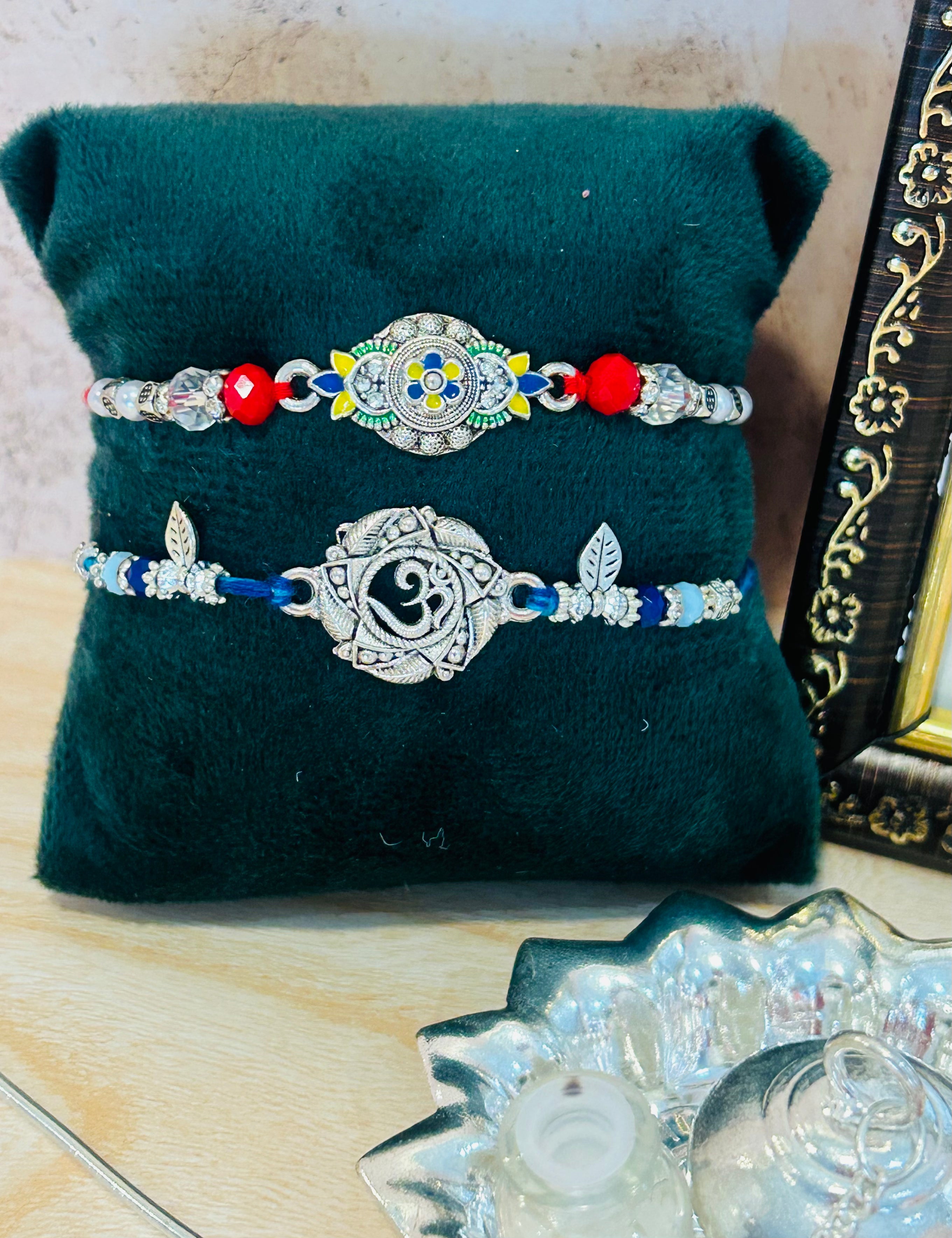 Set of 2 Rakhis – one with Om charm and one with colorful designer charm, with roli chawal pack – Wrap Shap Rakhi Collection