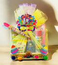 Holi gift hamper with Murukku, Dairy Milk Bites, Bhujia, juice, 4 packets of gulal, color smoke fog, snow spray, water balloons, and a decorative pichkari in a decorated pinewood basket.