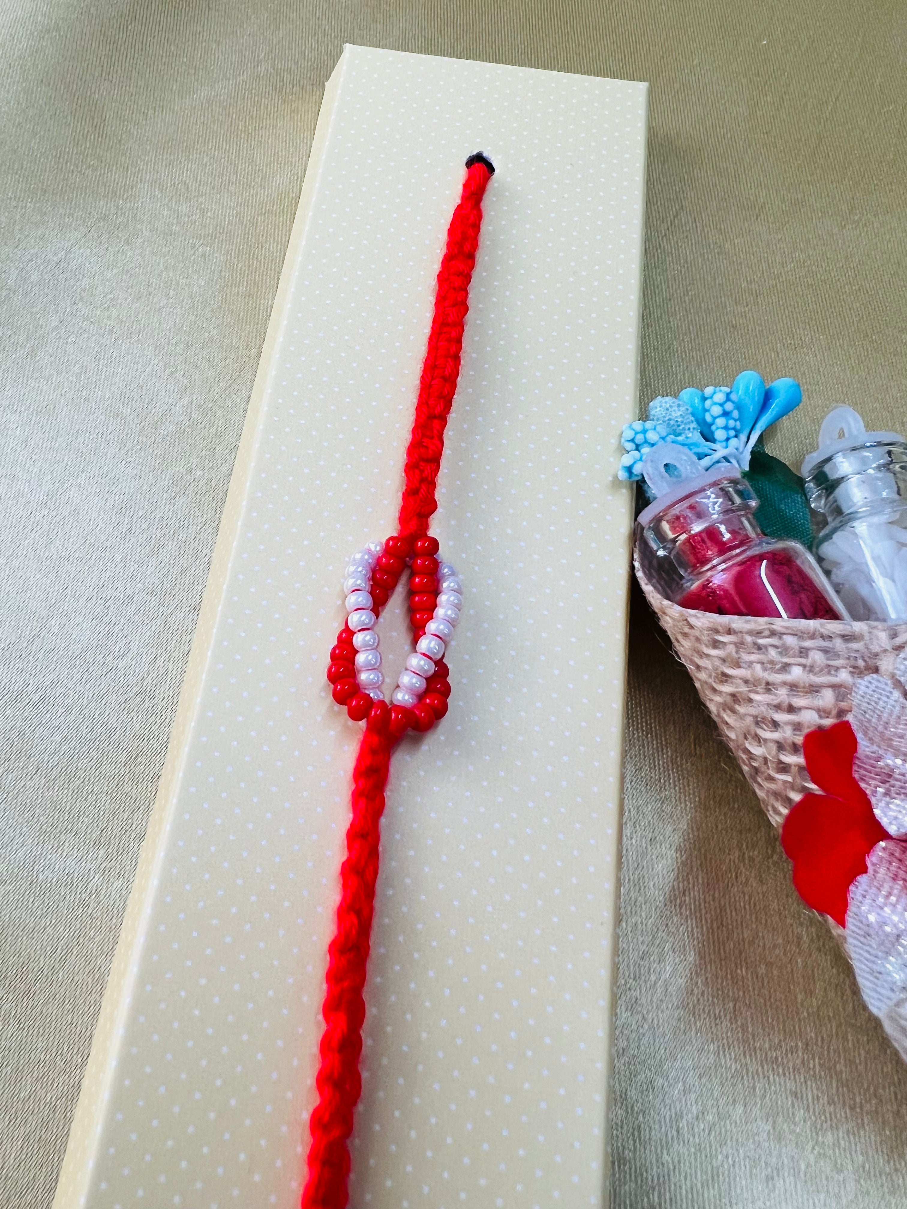 Wrap Shap RM801: Designer Beaded Rakhi with Red & White Infinity Symbol and Roli Chawal