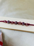 Wrap Shap RM811: Designer Crimson Beaded Rakhi with Decorative Elements and Roli Chawal