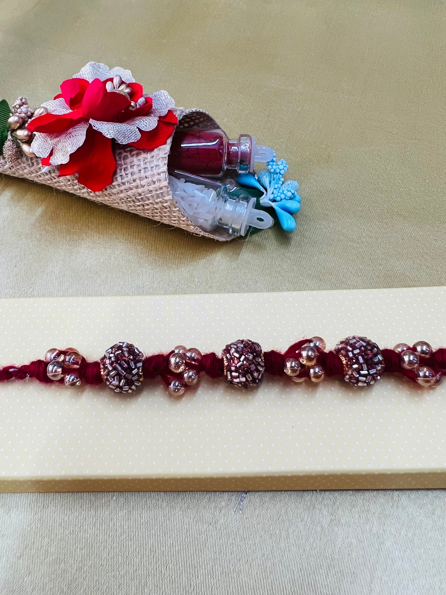 Wrap Shap RM811: Designer Crimson Beaded Rakhi with Decorative Elements and Roli Chawal