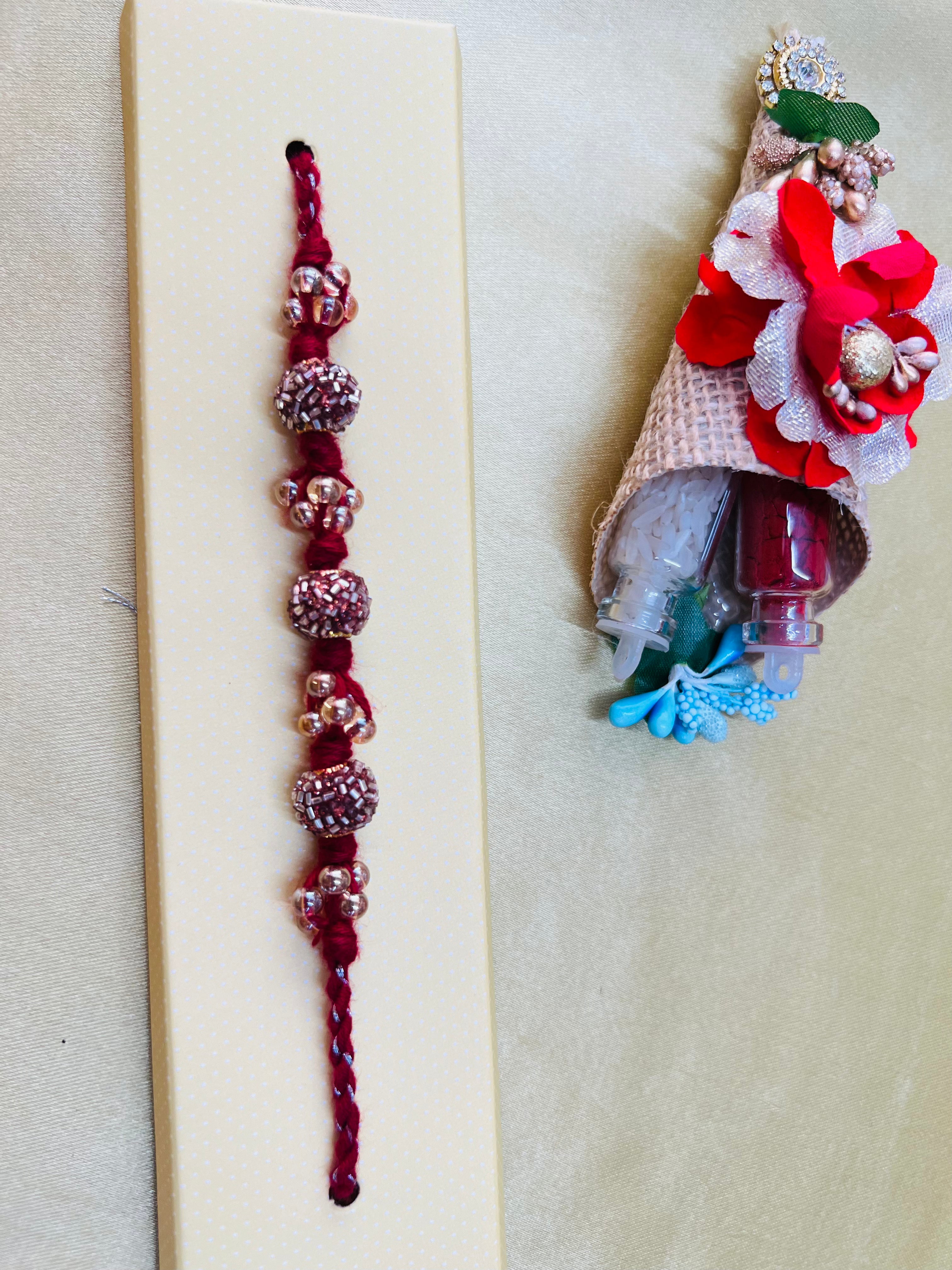 Wrap Shap RM811: Designer Crimson Beaded Rakhi with Decorative Elements and Roli Chawal