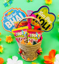 Holi hamper with mini gulal, Tong Garden party snack, Coke, and decorative pichkari in a colorful gift basket.