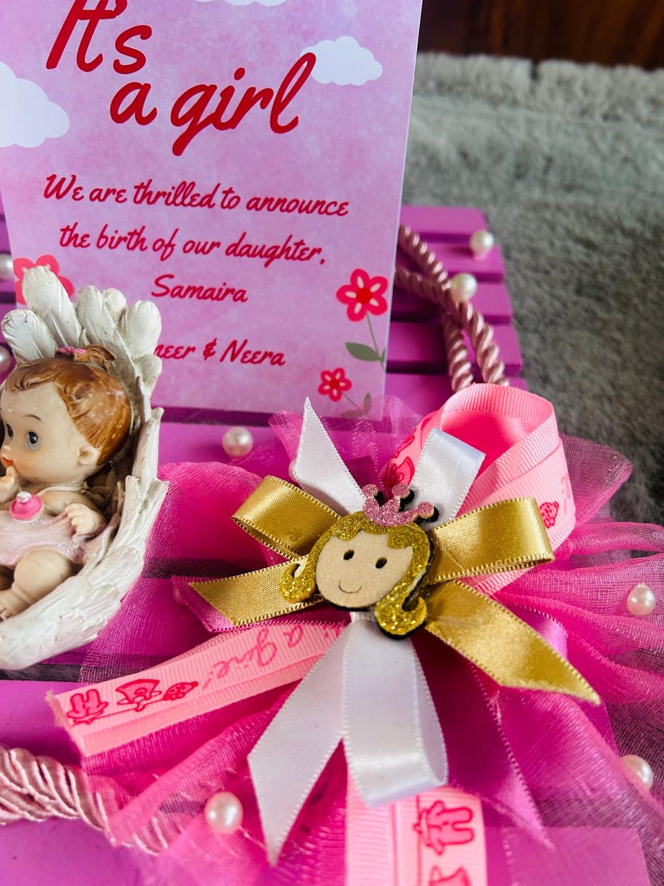 Baby shower gift with 'It's a girl' card, doll, and decorative ribbons on pink background