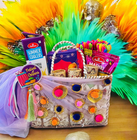 A beautifully decorated rafia basket containing Thandai, Gujia, Mathri, herbal gulal, and water balloons for Holi celebrations.