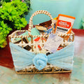 A decorated rafia basket containing various gourmet treats and a personalized message card, arranged for a newborn announcement.