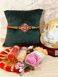 Diamond-shaped red enamel rakhi with floral pattern, green crystal beads, and golden accents – Rakhi Design 7339 from Wrap Shap.