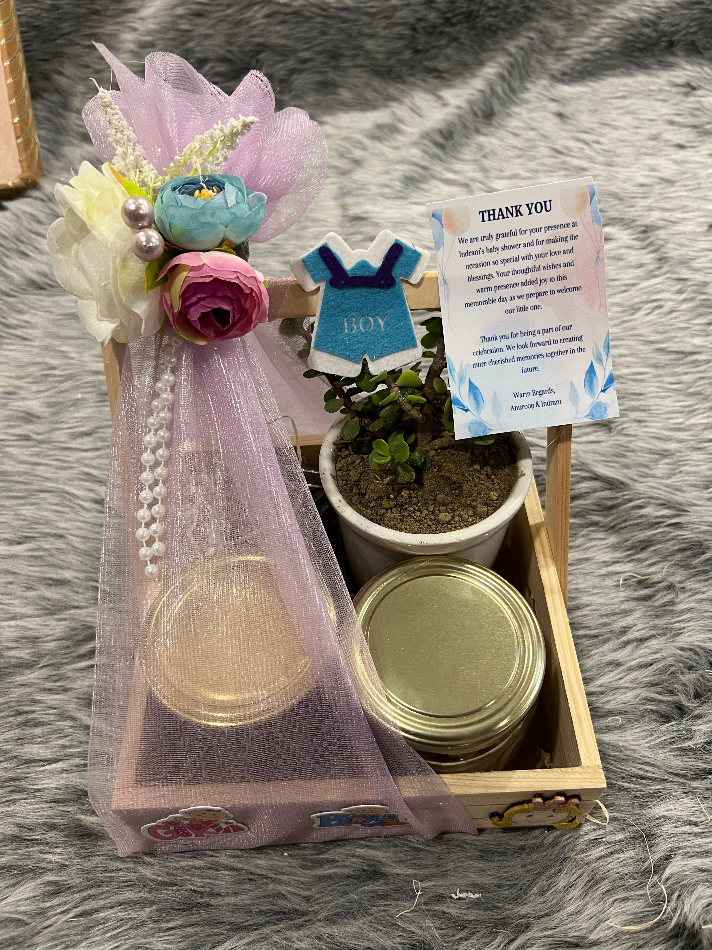 A wooden gift basket containing chocolate cookies, a brownie, almonds, and a jade plant, with a 'Thank You' note and a baby-themed decoration.