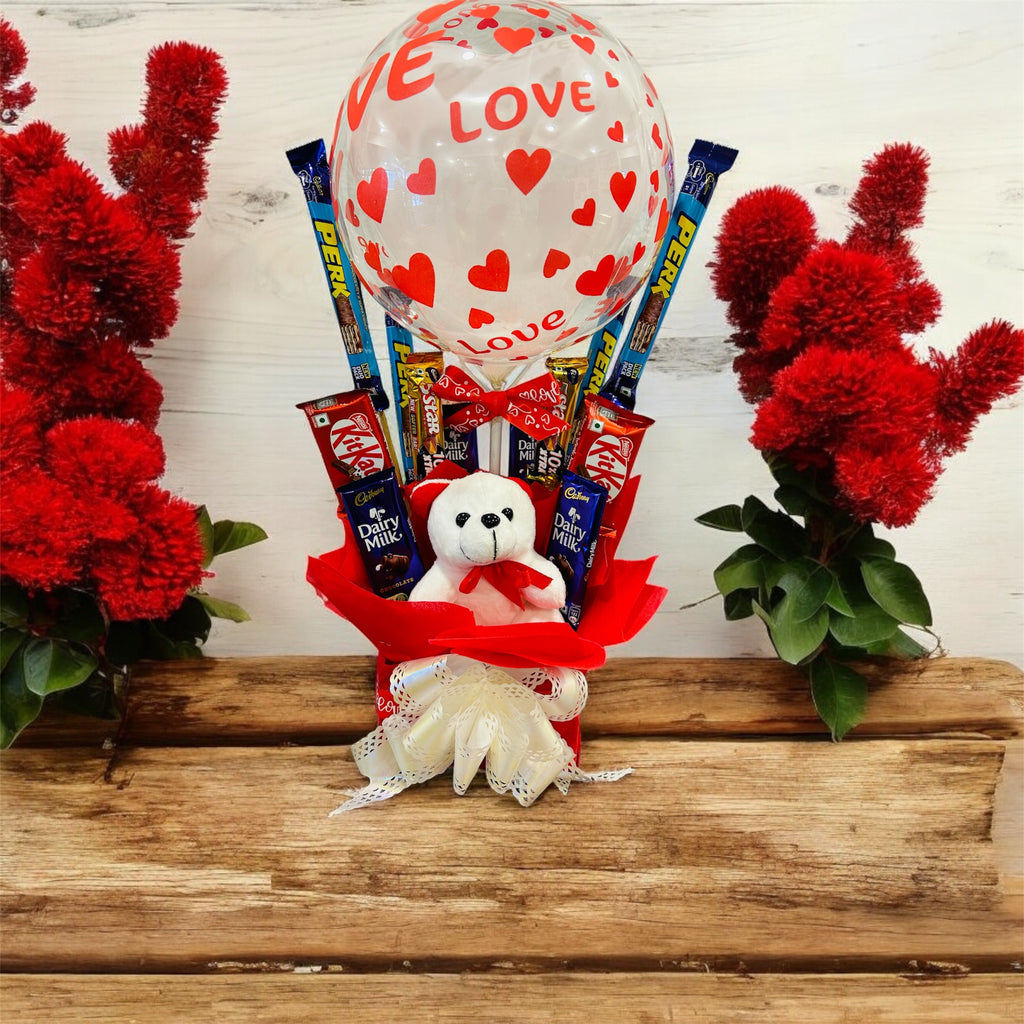 Love-themed transparent balloon hamper with a teddy bear and chocolates, perfect for romantic occasions like Valentine’s Day, anniversaries, and weddings.