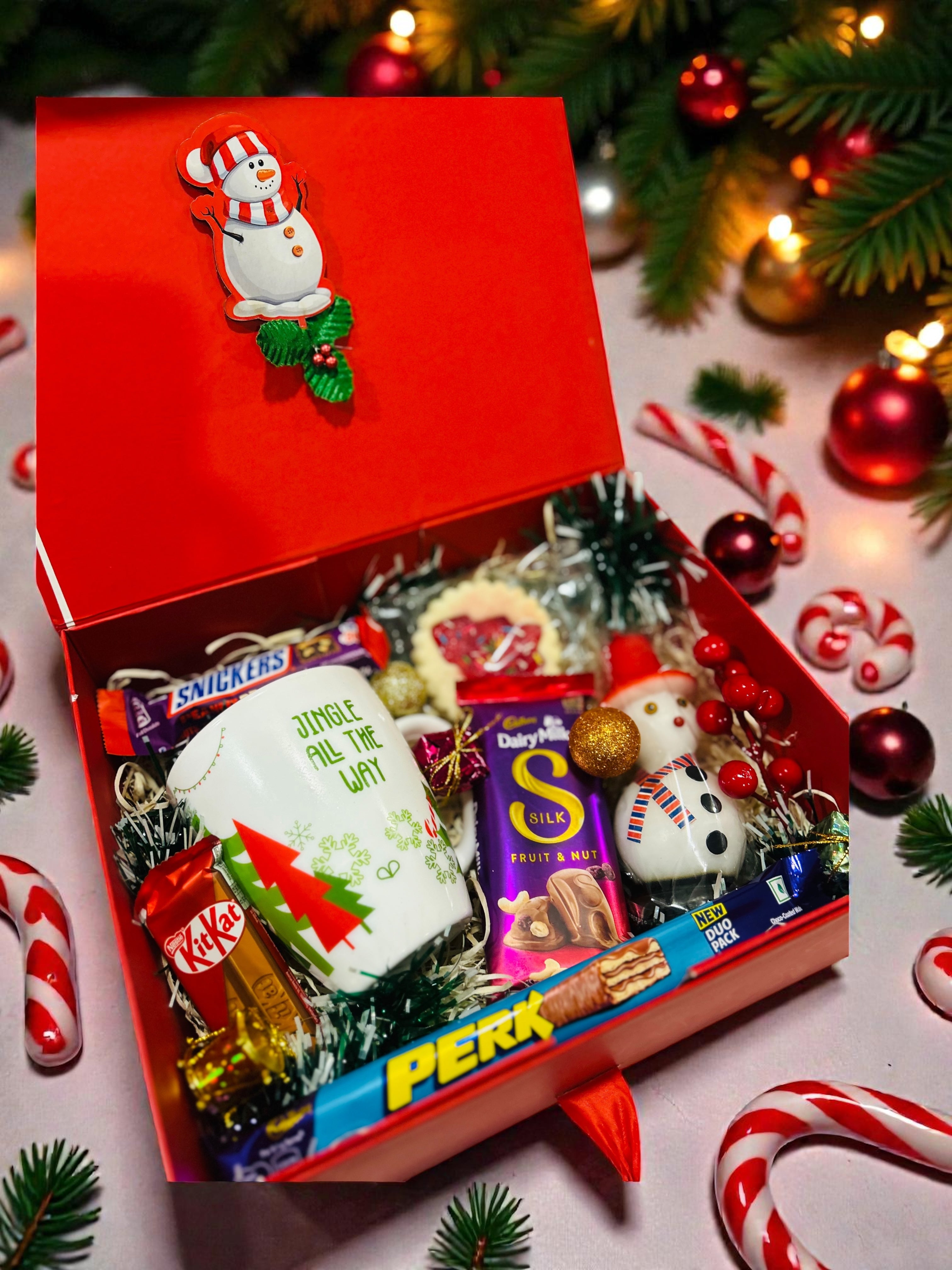 Christmas gift hamper in red gift box with festive mug, candle, cookies and chocolates.