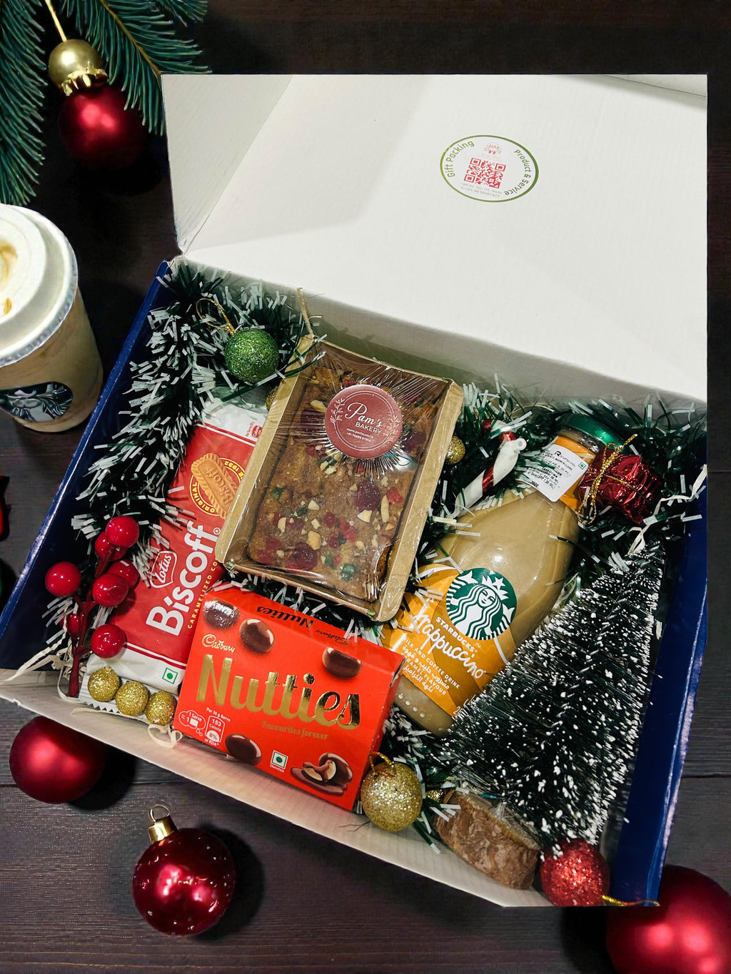 Christmas gift hamper with Starbucks coffee, plum cake, Lotus Biscoff and festive décor in gift box.
