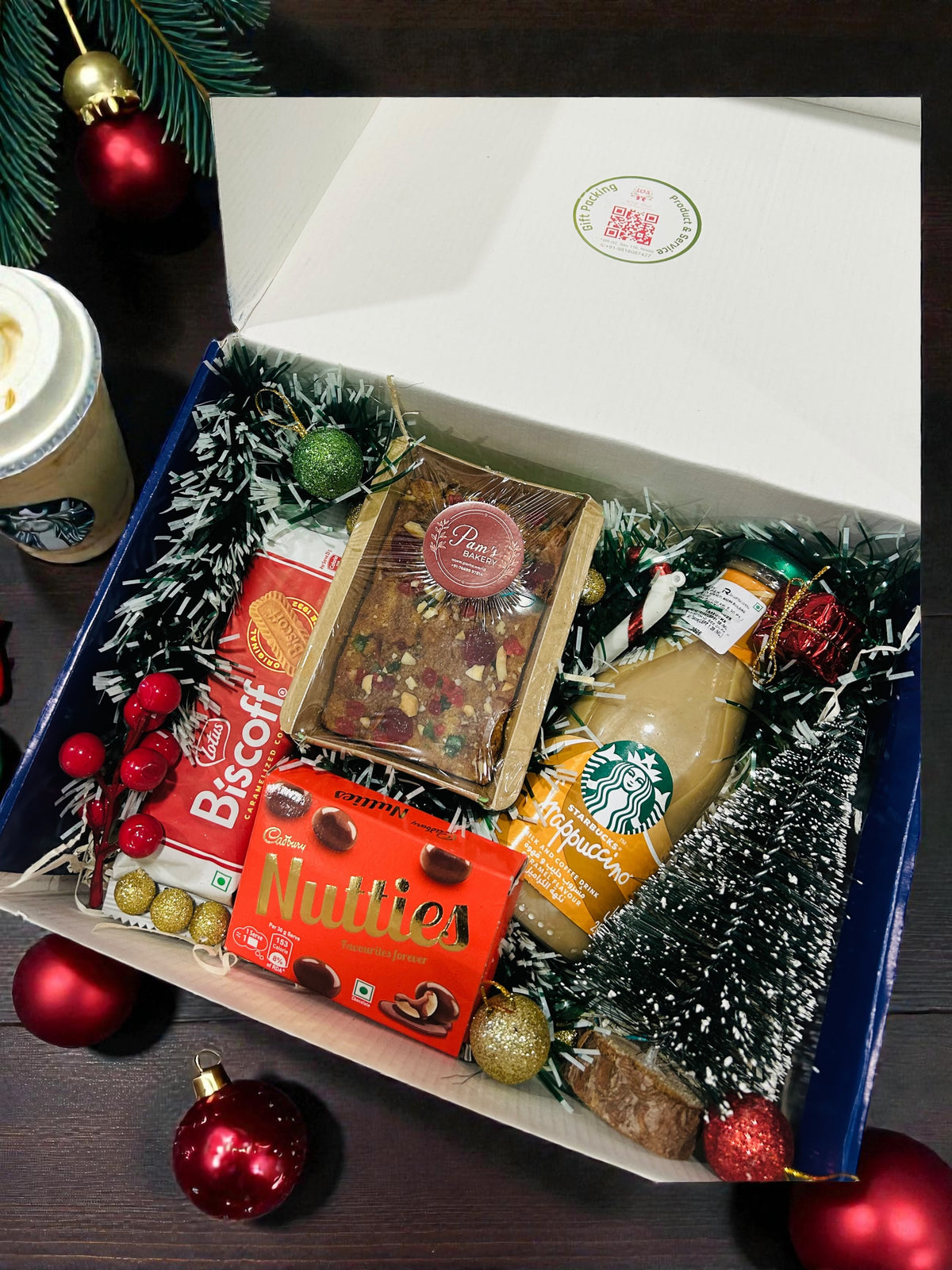 Christmas gift hamper with Starbucks coffee, plum cake, Lotus Biscoff and festive décor in gift box.