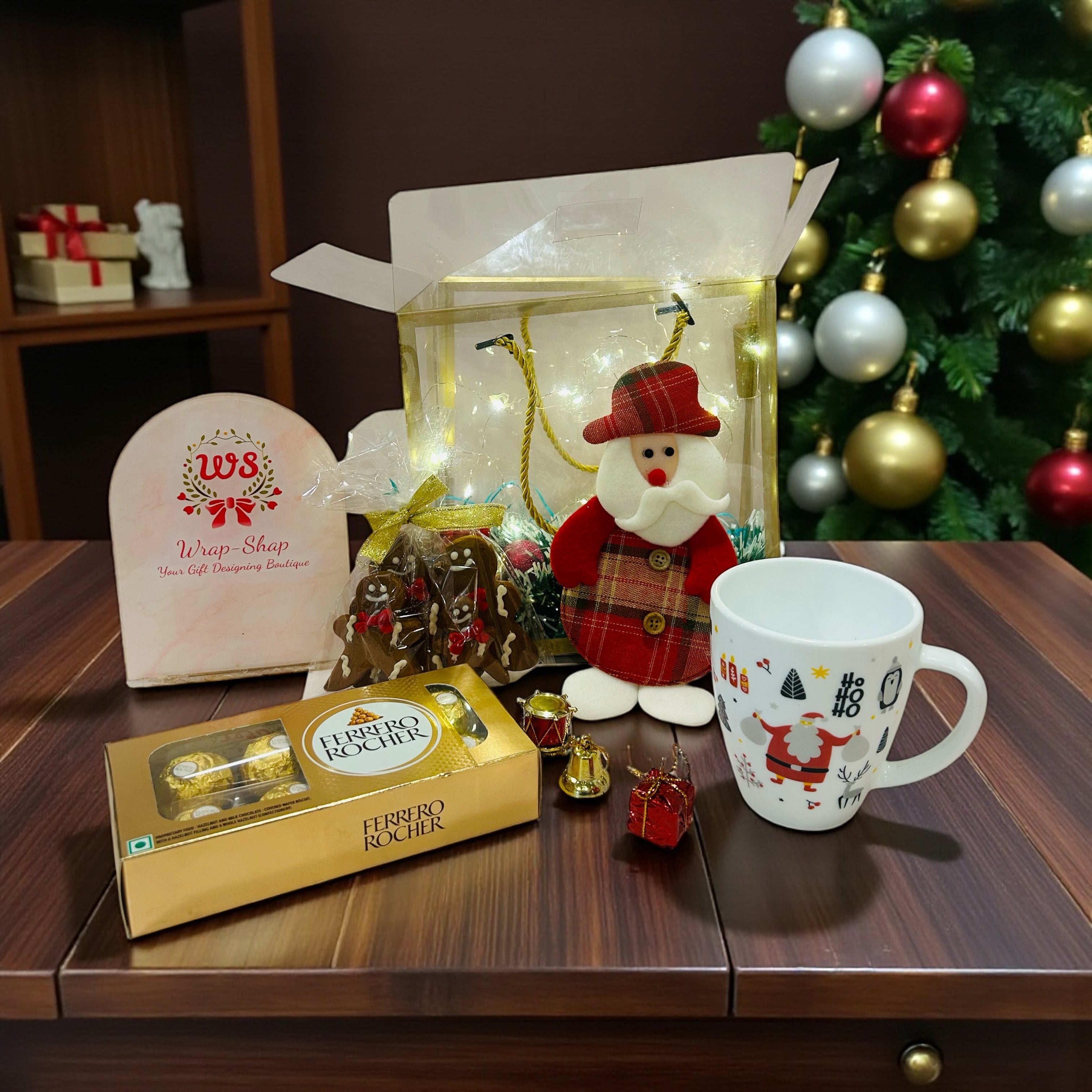 Christmas hamper in transparent bag with Ferrero Rocher, Christmas mug, gingerbread cookies and Santa hanging.