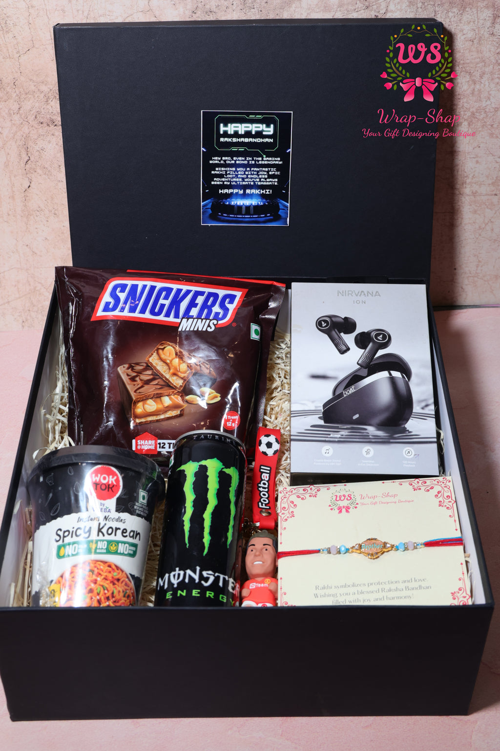 Wrap Shap gaming Rakhi hamper with Boat earpods, Korean noodles, energy drink, football keychain, Snickers chocolates and Rakhi in rigid gift box