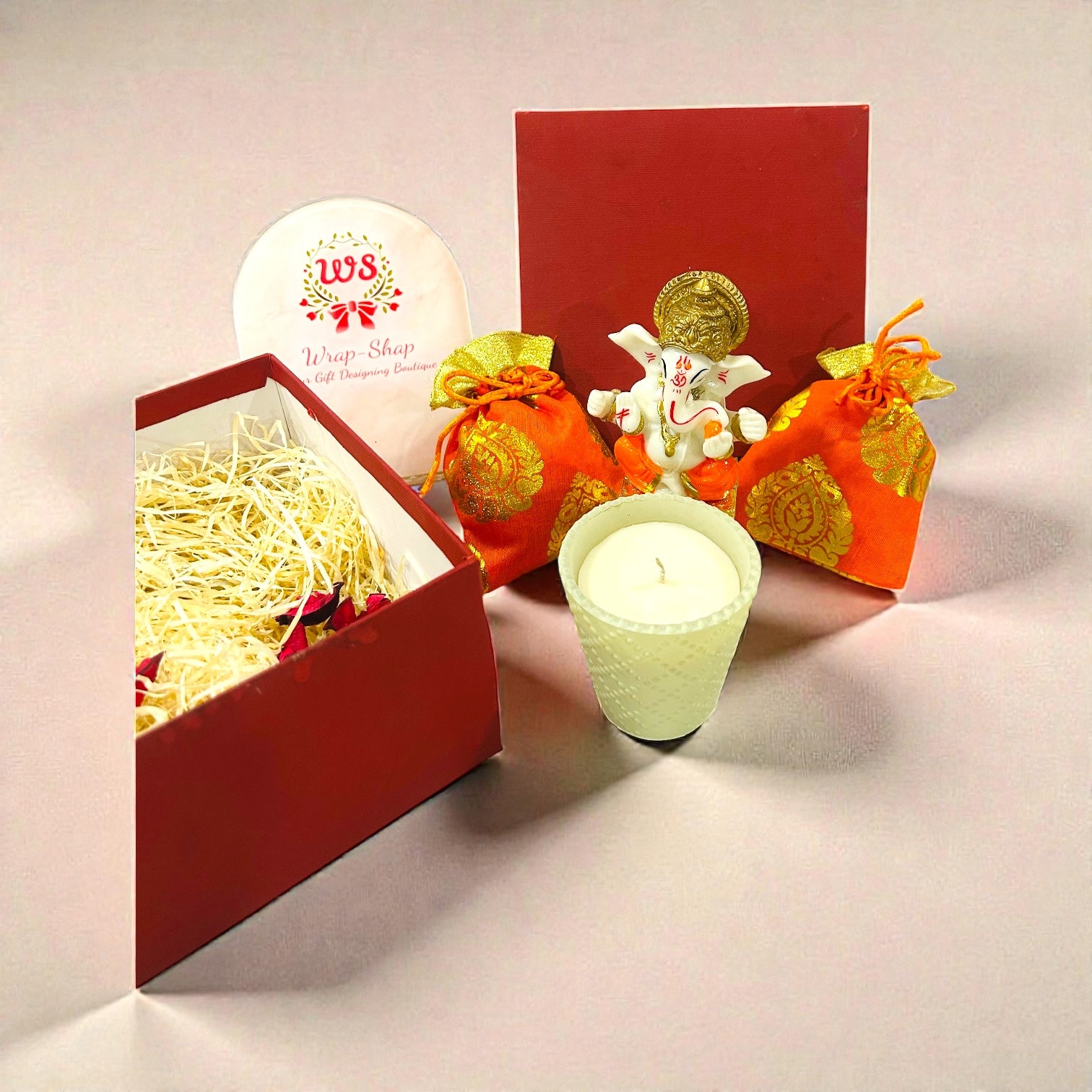 Premium wedding return gift featuring Ganesh statue, candle and cashew almonds in potli.