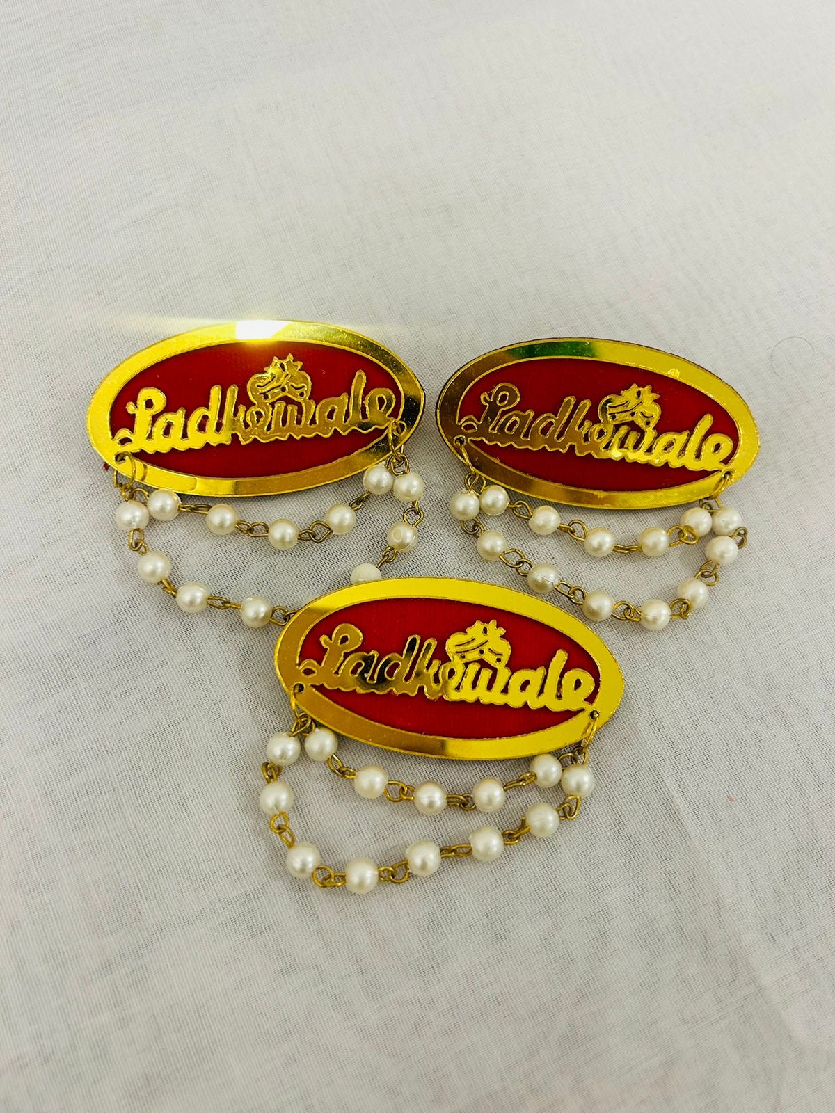 Elegant red & golden Ladkewale brooch featuring laser-cut acrylic “Ladkewale” text and pearl chain, perfect for groomsmen, groom’s family, and wedding guests at mehendi, sangeet, and wedding ceremonies.