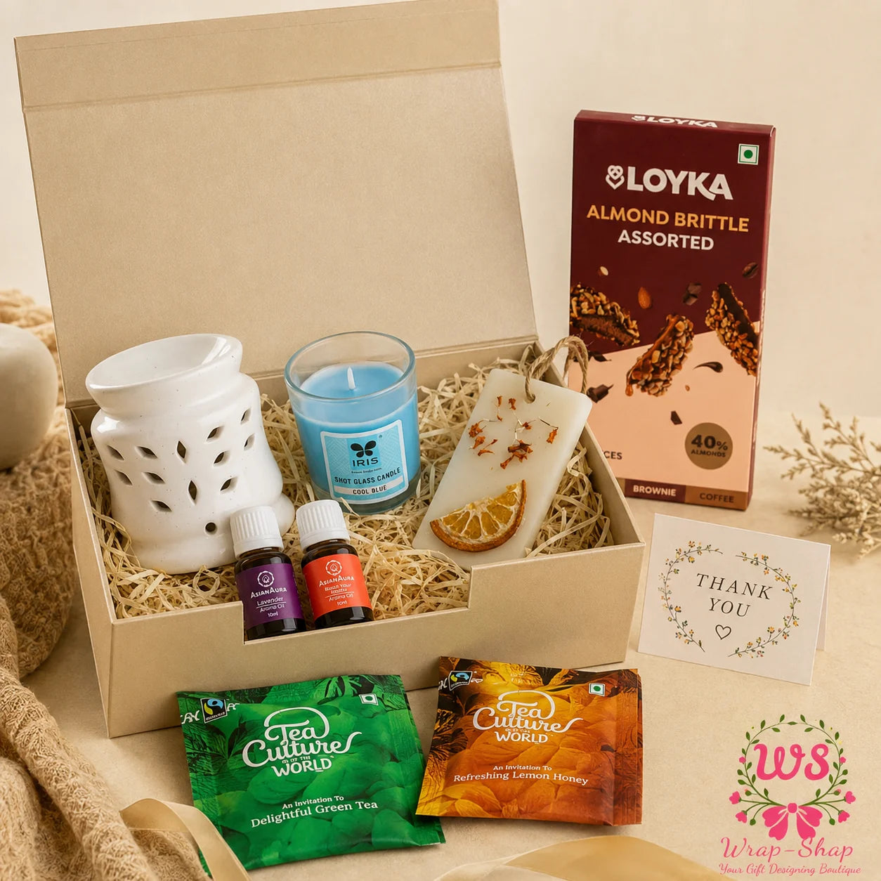 Luxury Aromatherapy Gift Hamper by Wrap Shap featuring a mini electric aroma diffuser, two essential oils, scented candle, wax tablet, herbal tea bags, Loyka Almond Brittle, thank-you tag, and premium gift box for wellness, home décor, and festive gifting.