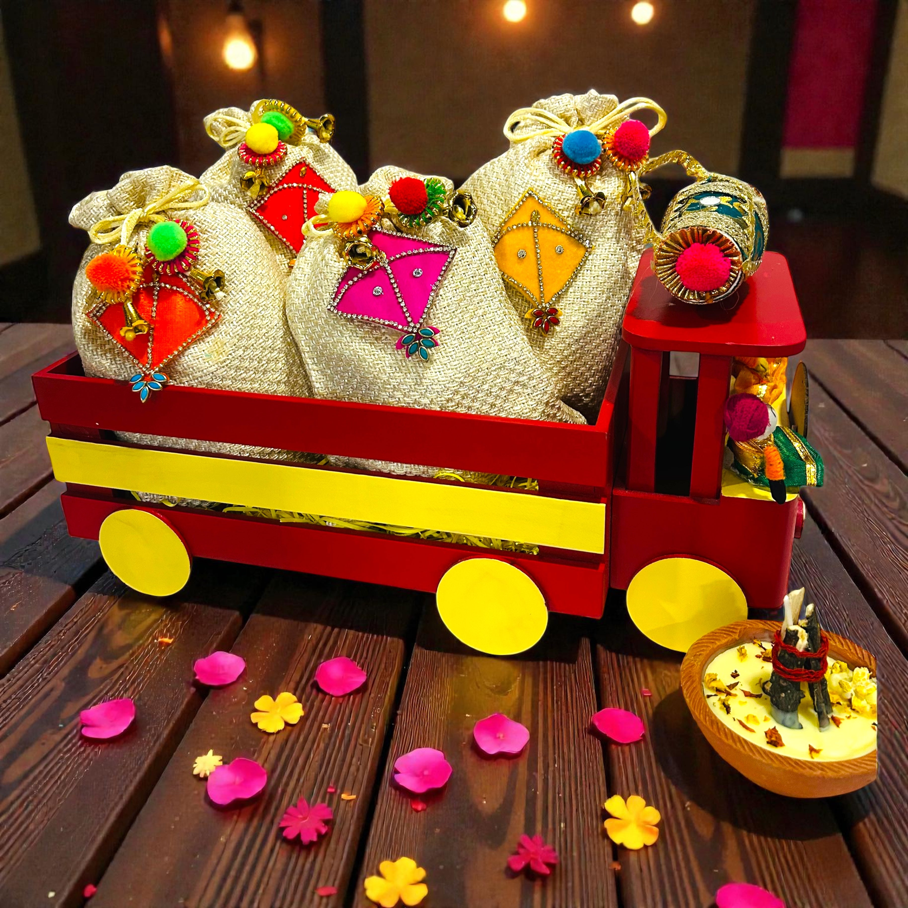 Wooden truck shape Lohri gift hamper with gajak, revdi, moongfali and popcorn in kite-decorated jute potlis.