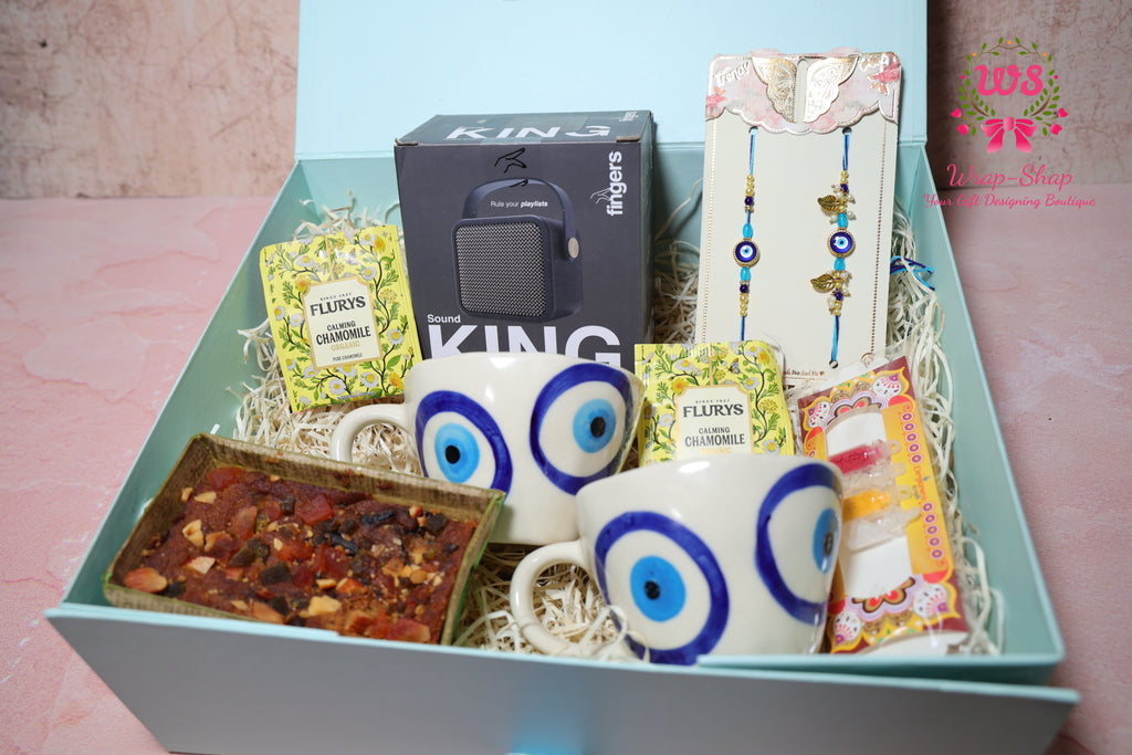 Bhaiya Bhabhi Rakhi hamper with evil eye tea cups, Bluetooth speaker, tea bags, tea cake and evil eye Rakhi set in a gift box by Wrap Shap