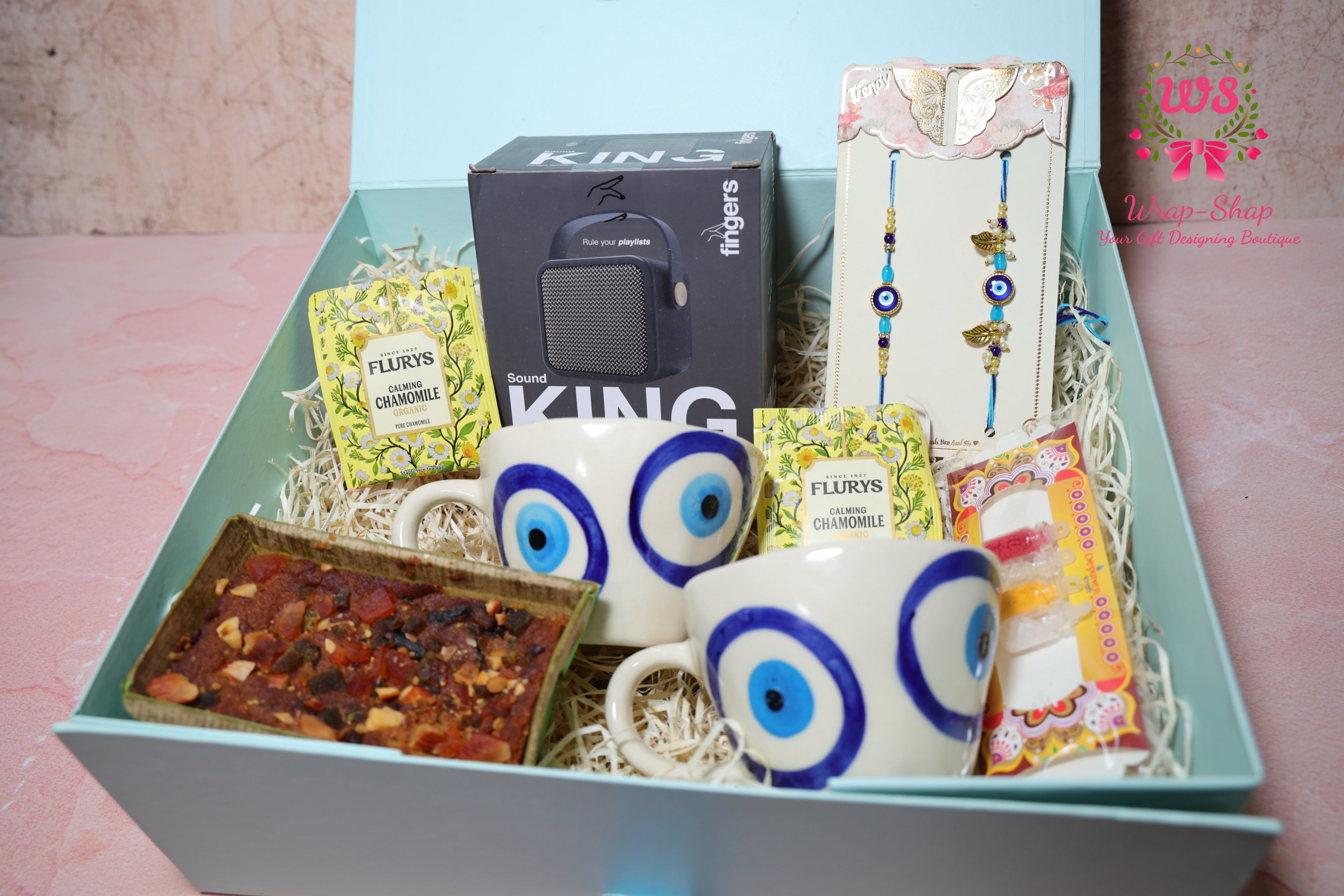 Bhaiya Bhabhi Rakhi hamper with evil eye tea cups, Bluetooth speaker, tea bags, tea cake and evil eye Rakhi set in a gift box by Wrap Shap