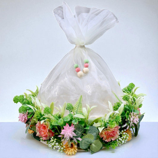 11-inch round gift basket decorated with artificial flowers, green leaves, and net cover, ideal for Indian festivals and gift hampers – by Wrap Shap